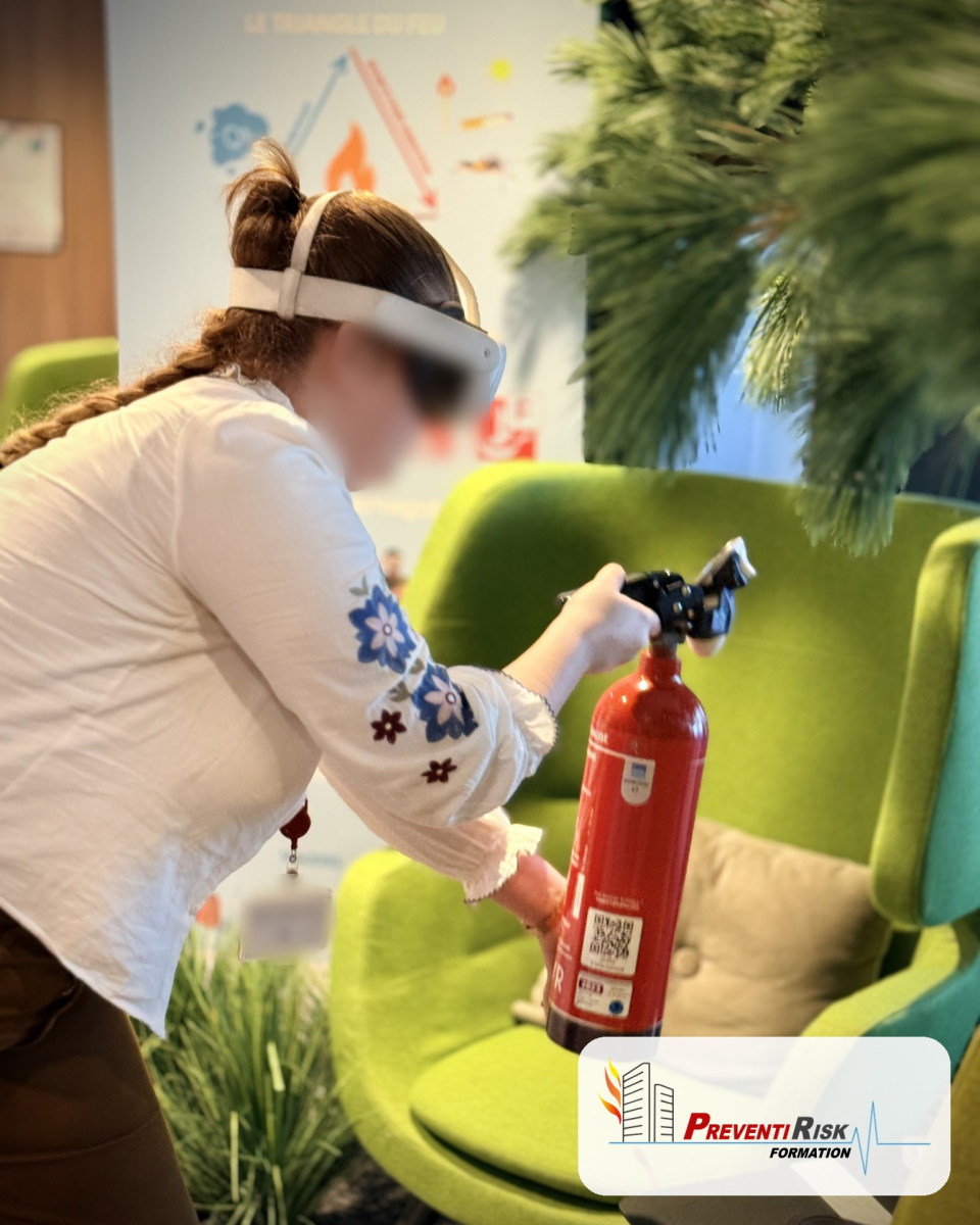 Plan rapproché d'une participante équipée d'un casque de réalité augmentée. Elle tient un extincteur rouge et vise un départ de feu simulé, dans un espace de bureaux avec fauteuils verts.